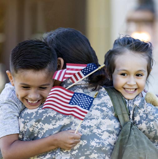 A woman in fatigues hugging two children.