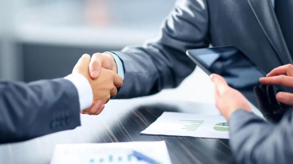 Two people shaking hands over a table with papers.